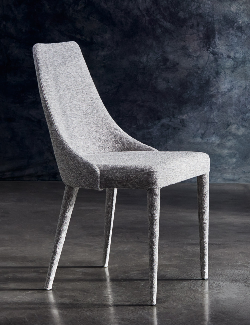 Sedia di design Evelin Julia Italia rivestita in tessuto, scatto lifestyle in studio con fondo scuro